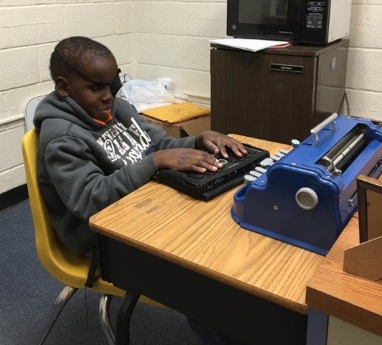 Mo is using a Perkins Braille Writer and BrailleNote Apex to complete a quarterly math assessment. 