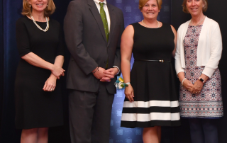 Julie Hummer, George Arlotto, Stacey Scofield, and Bonnie Johansen standing on stage at the Teacher of the Year banquet.