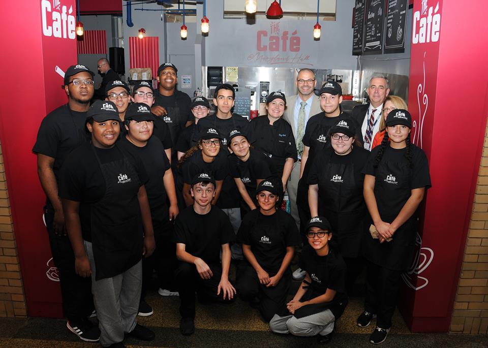 A large group of students stand in their employee uniforms at the Cafe at Maryland Hall
