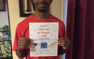 African american high school student holds a sign that says "Last first day of school" with the AACPS apple logo.