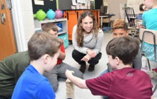 Teresa Beilstein sits with third grade students in a circle