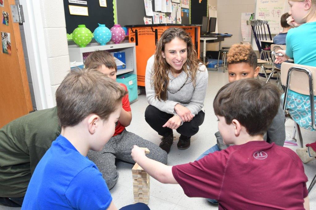 Teresa Beilstein sits with third grade students in a circle