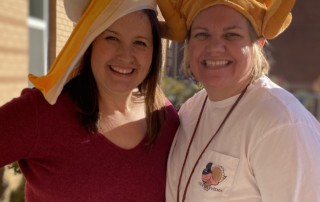 Casey Lee with a colleague, standing while wearing Thanksgiving hats.