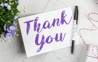 "Thank You"--purpose text on a card next to a pen and flowers